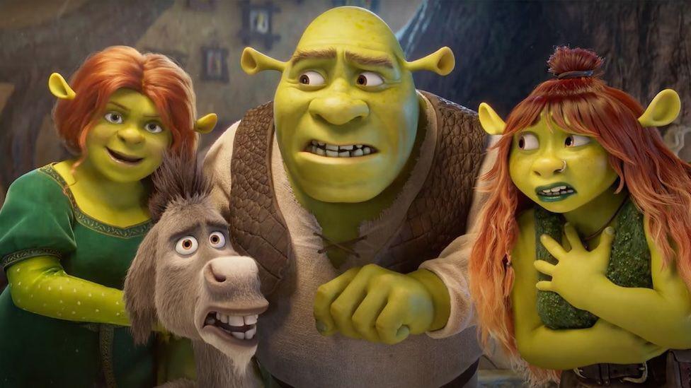 Screen grab from Shrek 5's trailer showing the green ogre Shrek in the middle, on his left is wife Fiona, also green with ginger hair and a green dress. On his right is his teenage daughter with ginger hair, the ends are ombre going into blonde. She has on green lipstick and green top. In the bottom left corner is Donkey looking puzzled. 