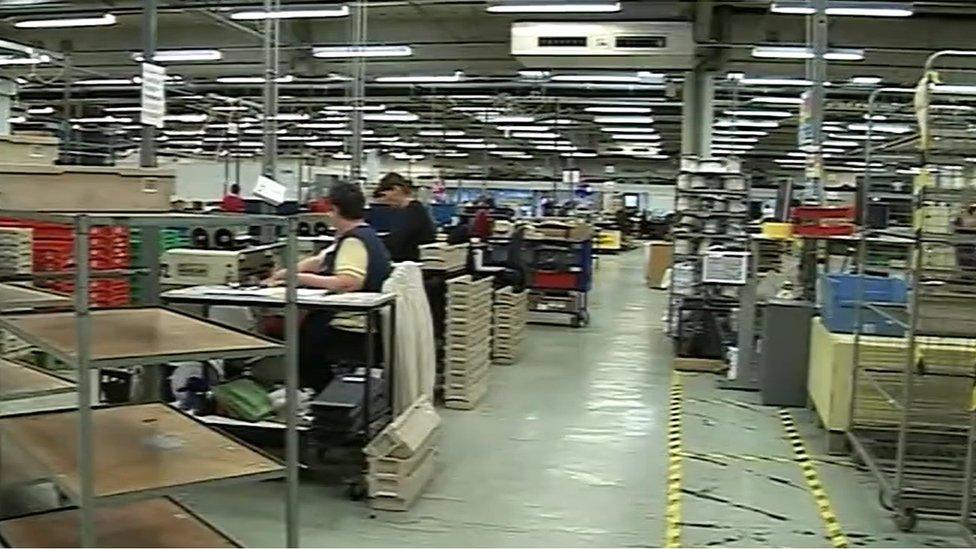 Packing room in large warehouse, showing workers with racks of products