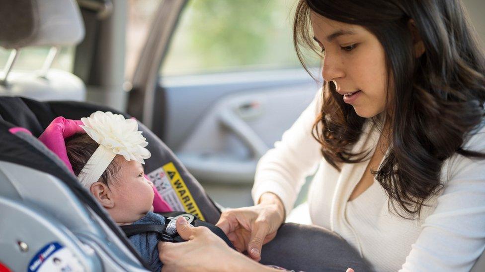 Mother strapping young baby girl into car seat