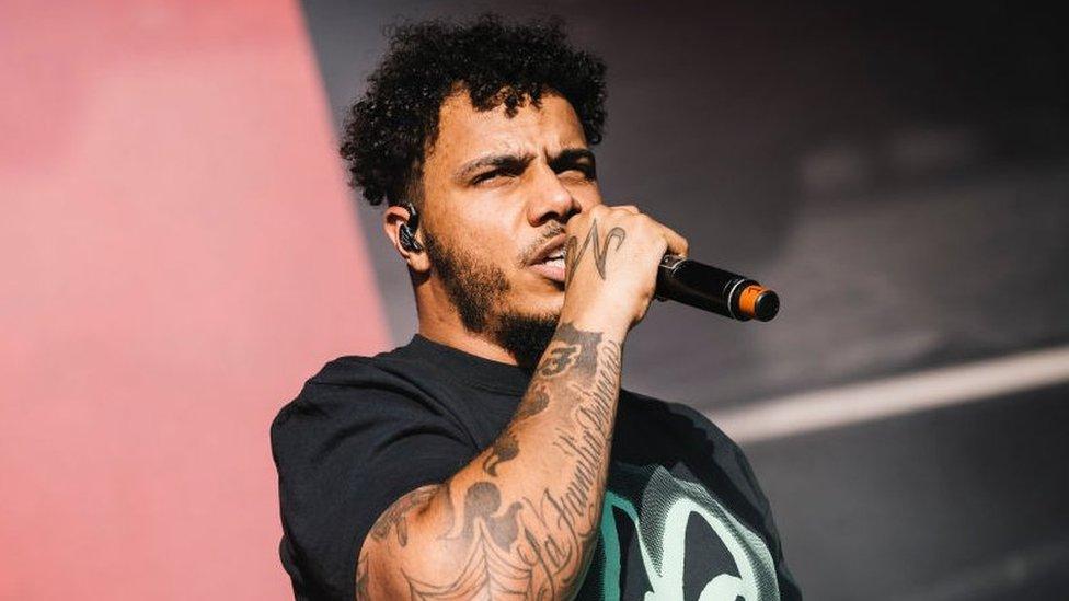 AJ Tracey performing at Laneway festival, he is wearing a black t-shirt and holding a microphone