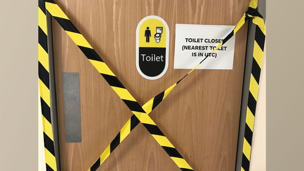 A toilet door with yellow and black tape across it and a sign saying "toilet closed nearest toilet is in UTC"