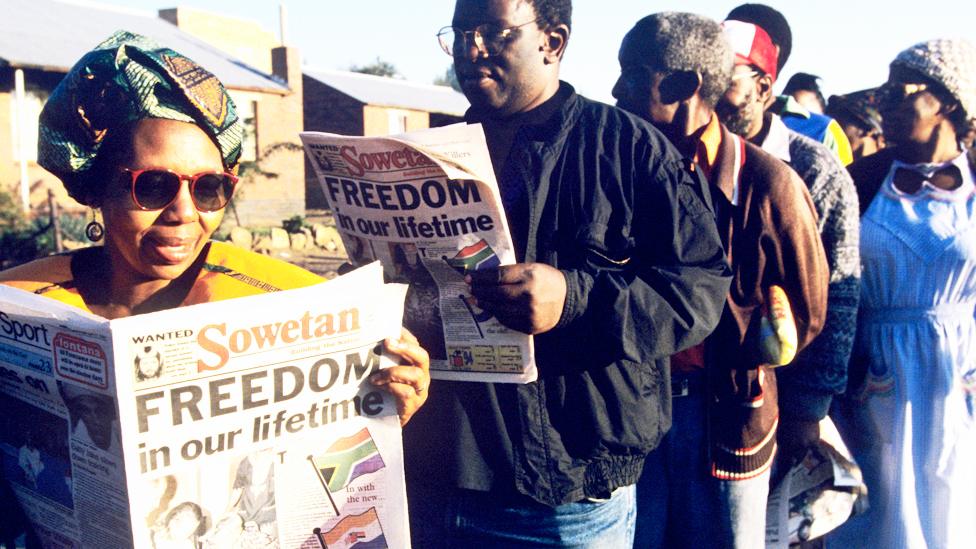 People line up to vote in the South Africa township of Soweto reading a paper with the headline "Freedom in our lifetime" - 27 April 1994