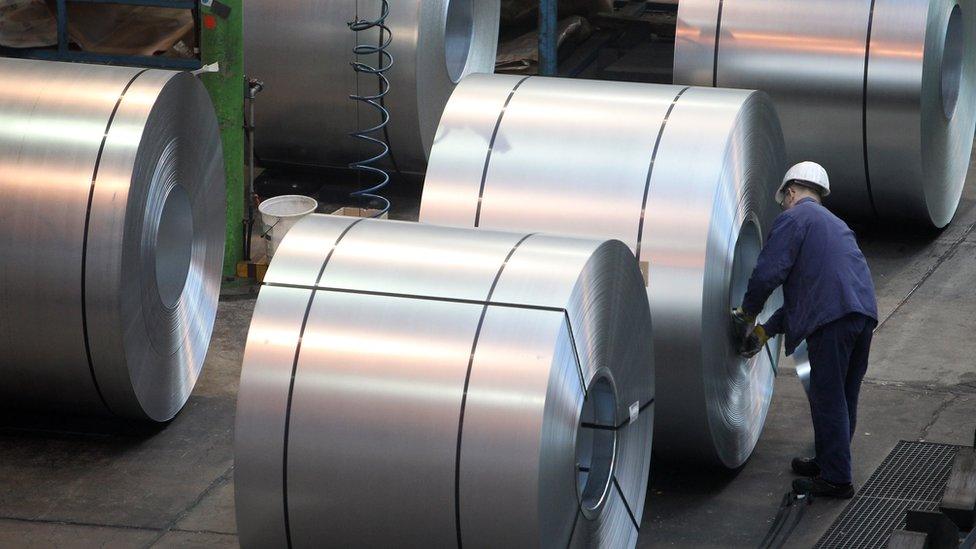 A worker inspects rolls of steel at a factory