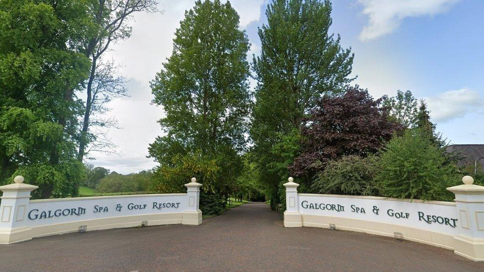 Google view of the Galgorm spa and golf resort, a white curved wall with text, with a brown driveway and large green trees