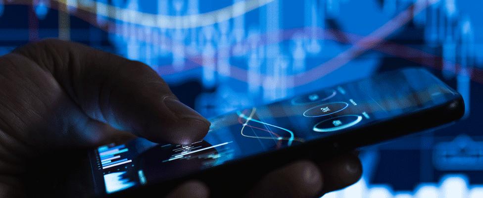 Man holding a phone with financial markets graphs on it