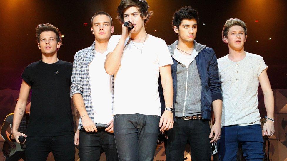 The five members of 1D together on stagem Harry sings into a microphone.