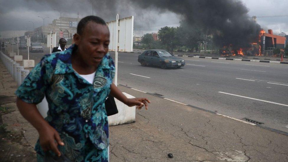 People walk past a fire service station set ablaze by members of the Shia Islamic Movement in Nigeria (IMN) during clashes with the police in the streets of Abuja on July 22, 2019.