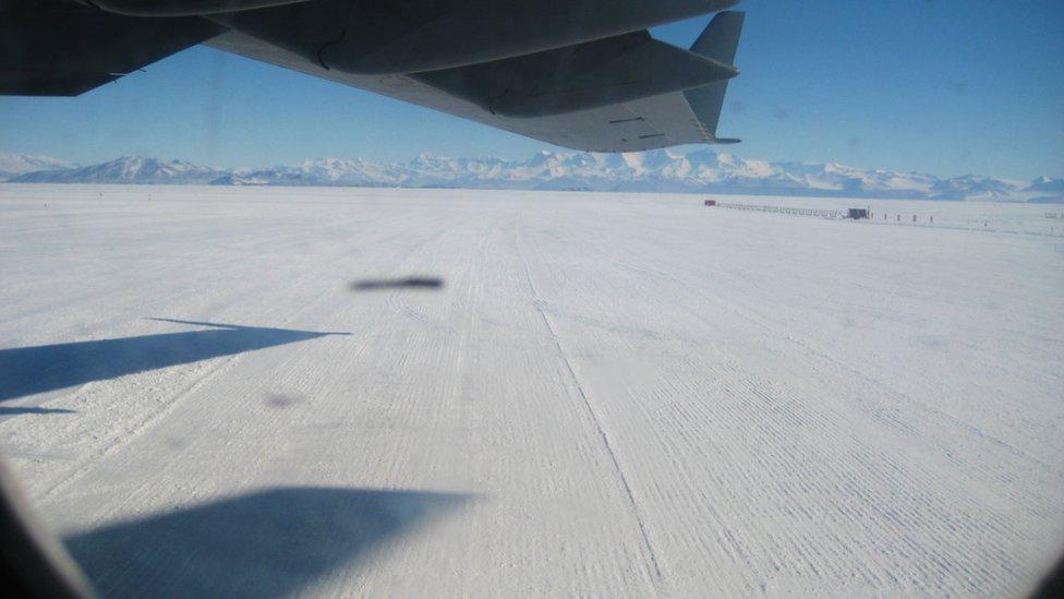 View from a plane window across a field of snow with distant mountains in the background