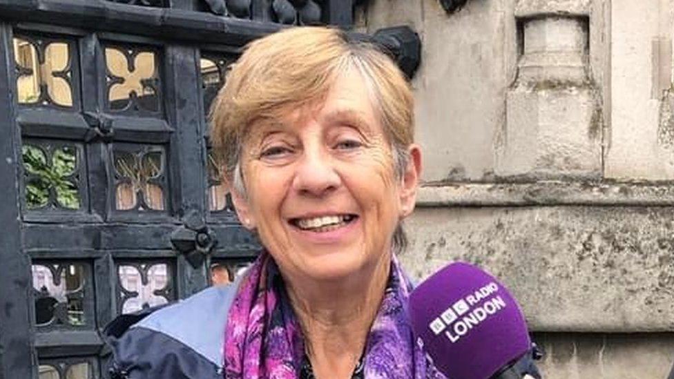 A woman standing in front of a building with a BBC London microphone being held out to her