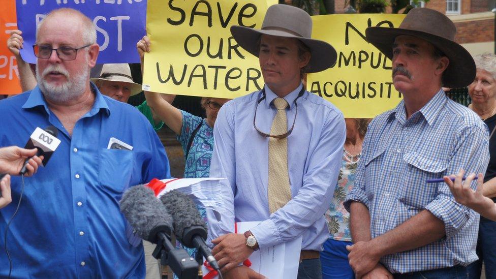 Three farmers at a protest with a placard behind them reading 'save our water'