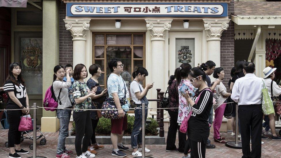 Visitors stand in a line outside retail stores at Walt Disney Co.'s Shanghai Disneyland theme park