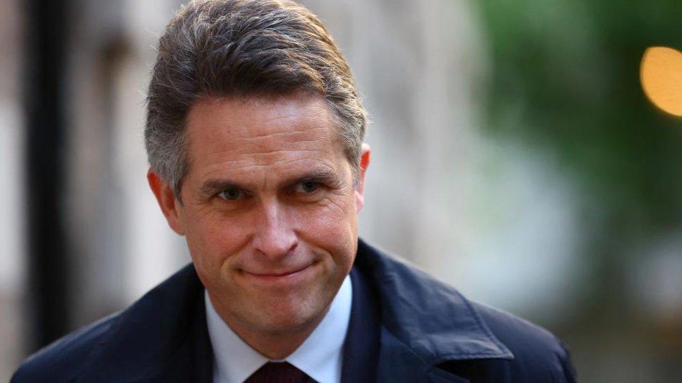 Sir Gavin Williamson smiles as he walks down a street