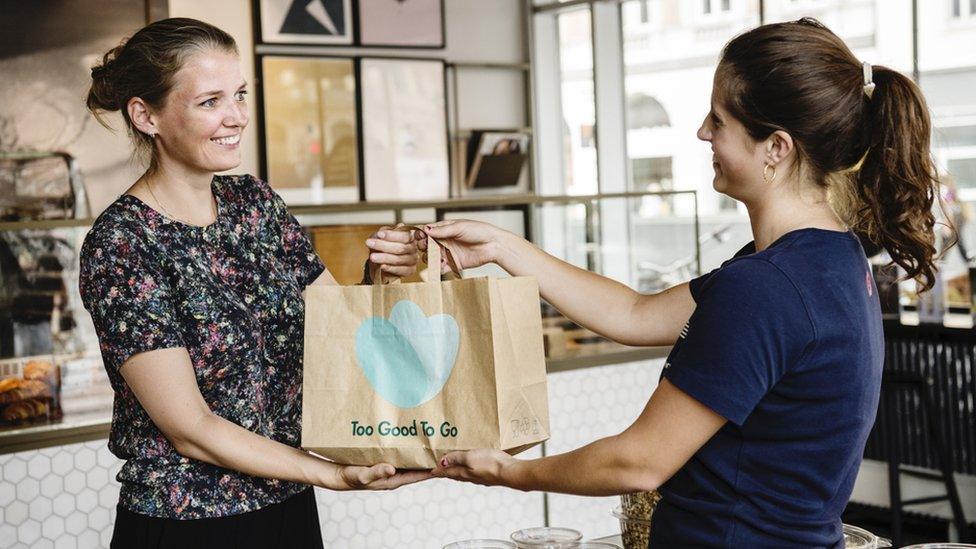 A shop giving a customer a Too Good To Go bag