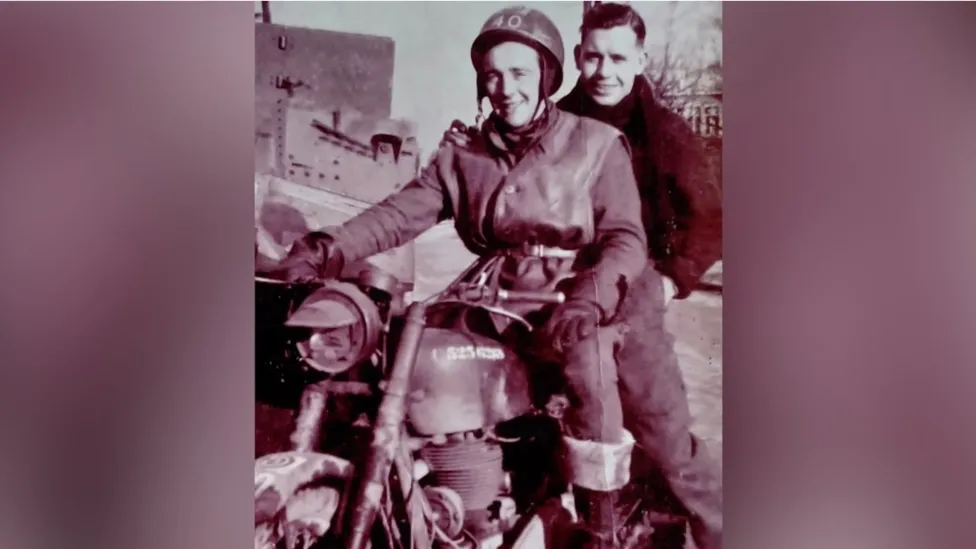 An old black and white photo from World War Two with Don riding a motorbike with a man, both smiling