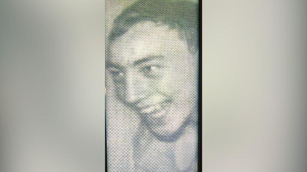 A grainy image of Michael Neill. It is black and white, he is smiling and looking to the left. It is blurred on either side.