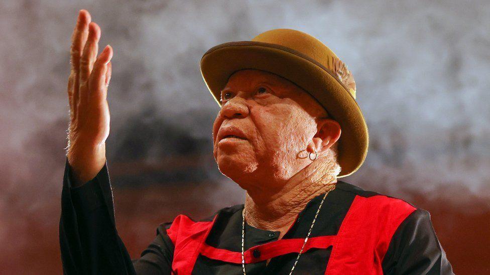 Salif Keïta giving a concert in Ankara, Turkey - 2022. He's wearing a beige bowler hat and a black and red outfit