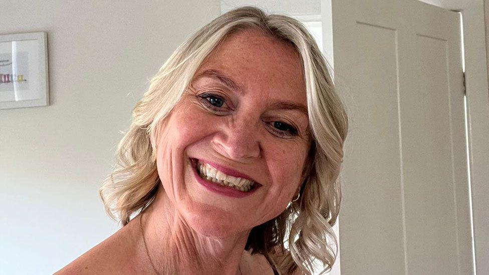 Amanda, who has blonde hair, smiles at the camera with her head tilted slightly to one side