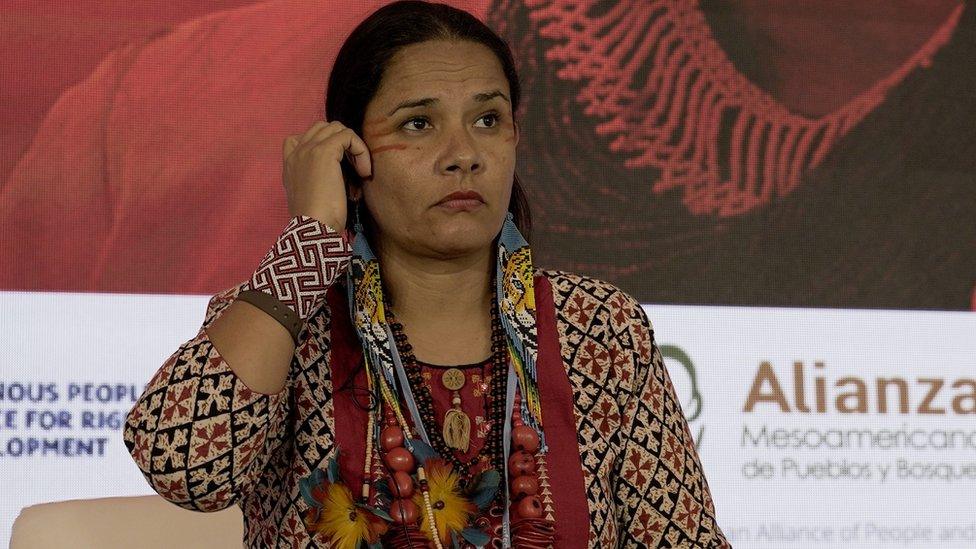 Shirley Djukurna Krenak sitting on a chair, tucking hair behind her ear