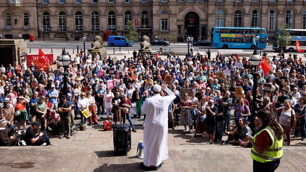 Adam Kelwick, an iman at Abdullah Quilliam Mosque dressed all in white, speaks to a large crowd of people during the Stand Up to Racism rally at St George’s Hall in Liverpoo