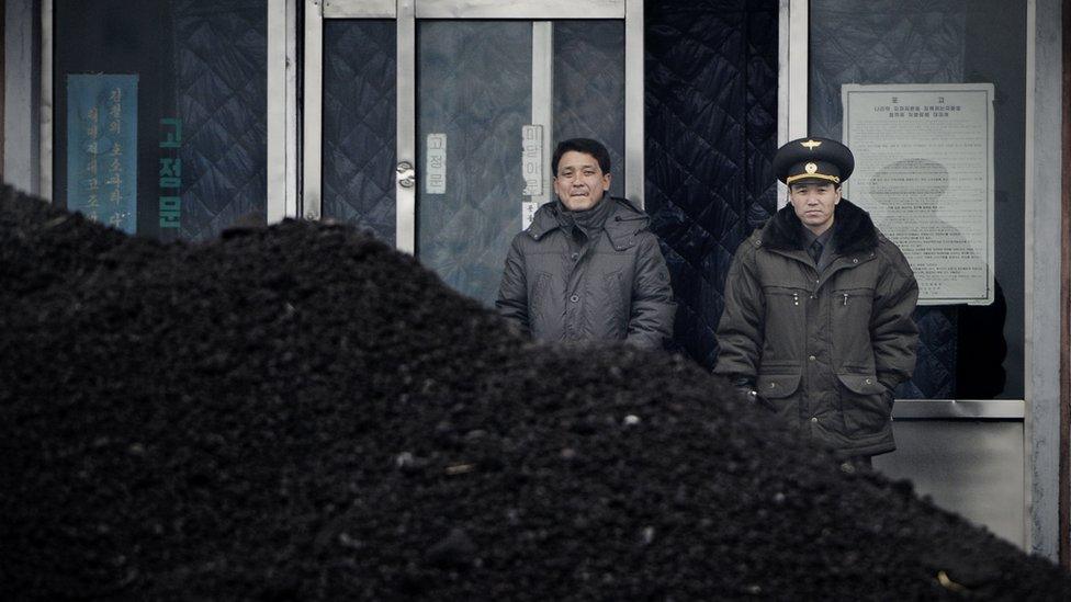 This picture taken on December 14, 2012 from China's northeastern city of Dandong, looking across the border, shows a North Korean military officer (R) and a North Korea man (L) standing behind a pile of coal along the banks of the Yalu River in the northeast of the North Korean border town of Siniuju.