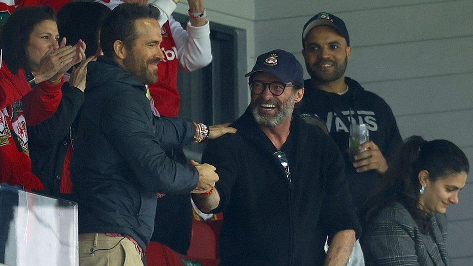 Ryan Reynolds shakes the hand of Hugh Jackman from the stands at the Racecourse Ground