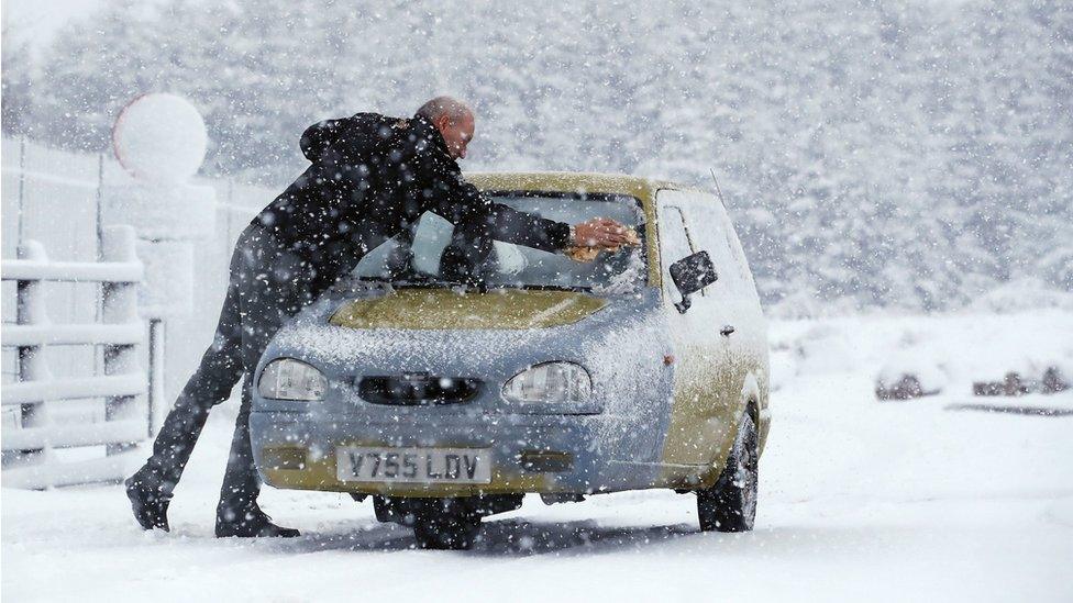 A man scrapes ice off his 3 wheel Reliant Robin in Cumbria