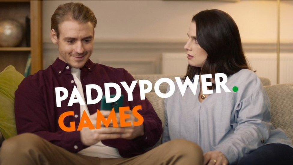 Still frame from Paddy Power advert showing a man smiling in to his mobile phone as his partner looks on incredulously