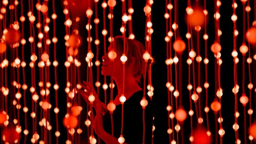 A woman stands among hundreds of suspended bright lights as part of an exhibition