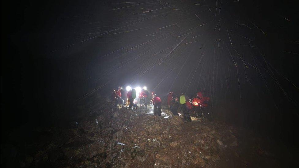 People in red coats with head torches walk through the dark and rain