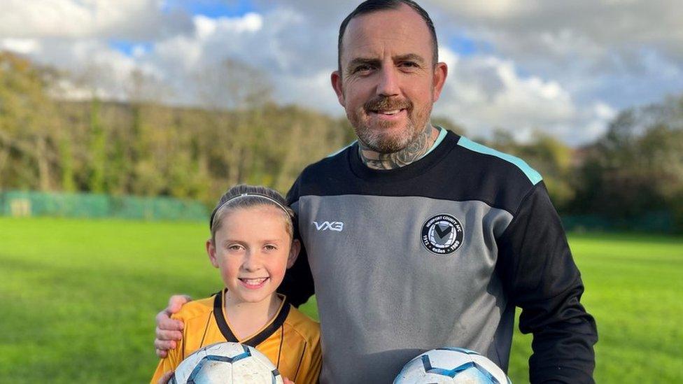 Matthew Evans with his arm around son Ollie in a field with both holding footballs