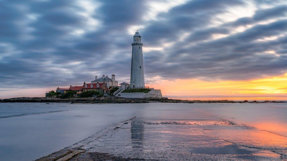 A lighthouse on a rock with the sunrise beyond it