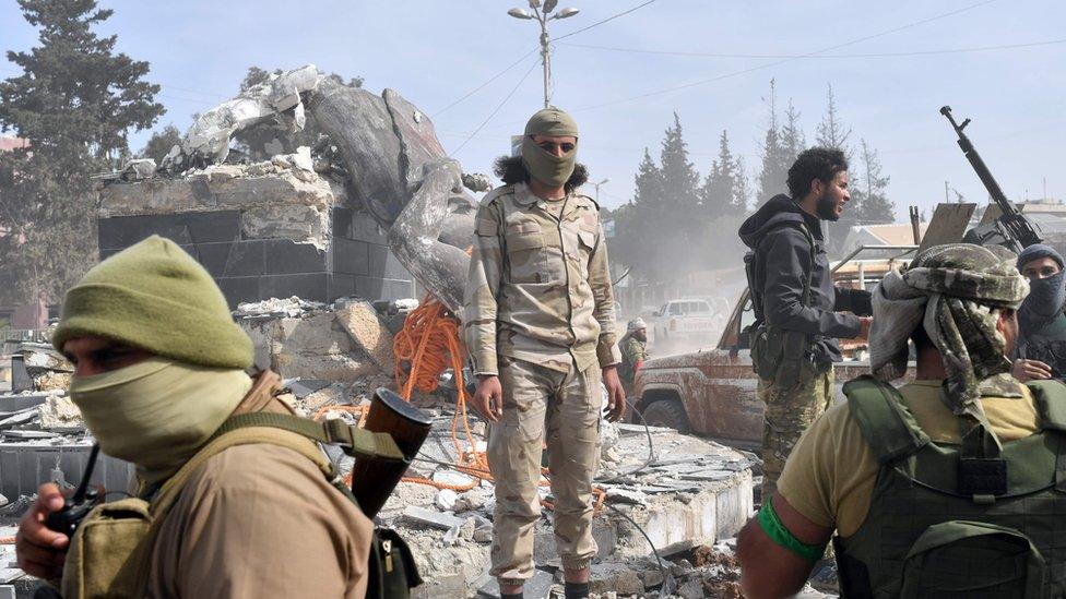 Turkish-backed Syrian rebels gather next to the destroyed Kawa statue in the city of Afrin in northern Syria on March 18, 2018