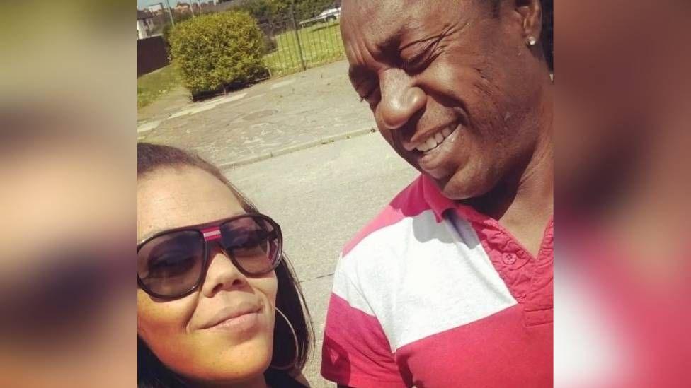 A selfie of Natalie and her dad Anthony, She is wearing sunglasses and has dark hair with some of it pulled back. Anthony is looking at his daughter and smiling, he has an earring and is wearing a red and white striped shirt.
