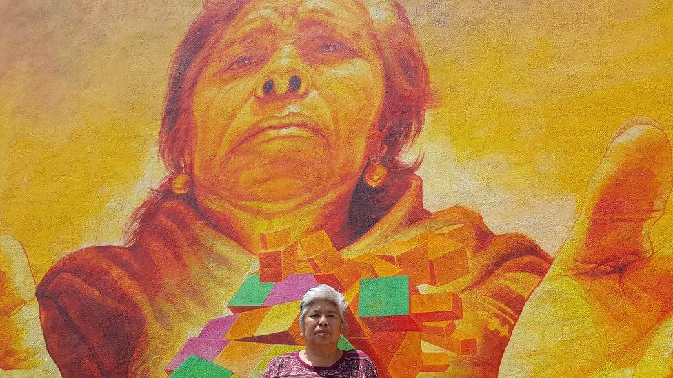 A local resident poses in front of the mural depicting her