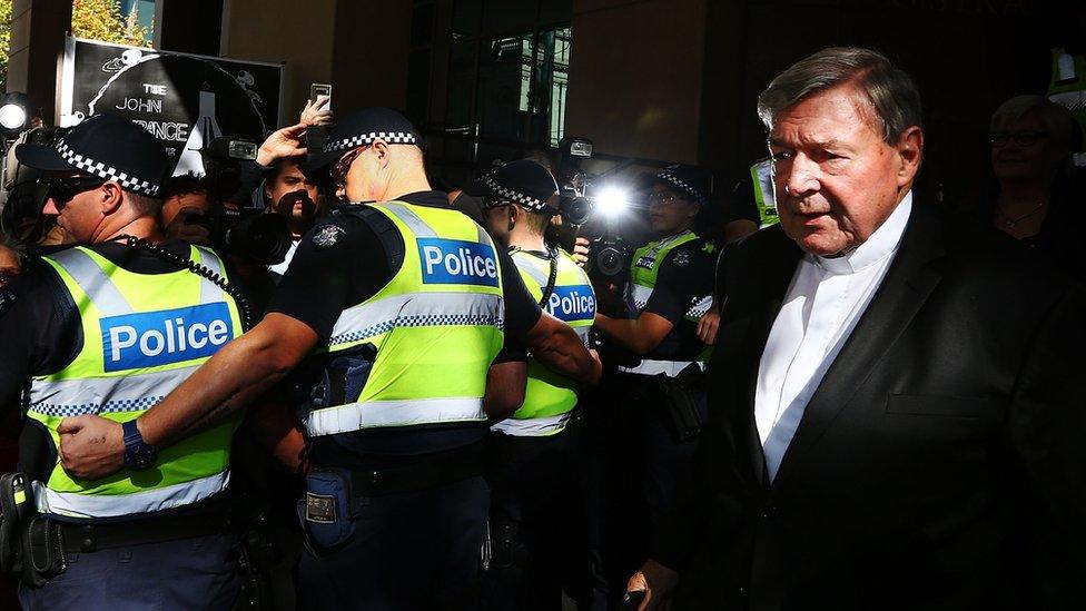 A line of police hold back media and spectators to allow George Pell to leave the Melbourne Magistrate's Court in May