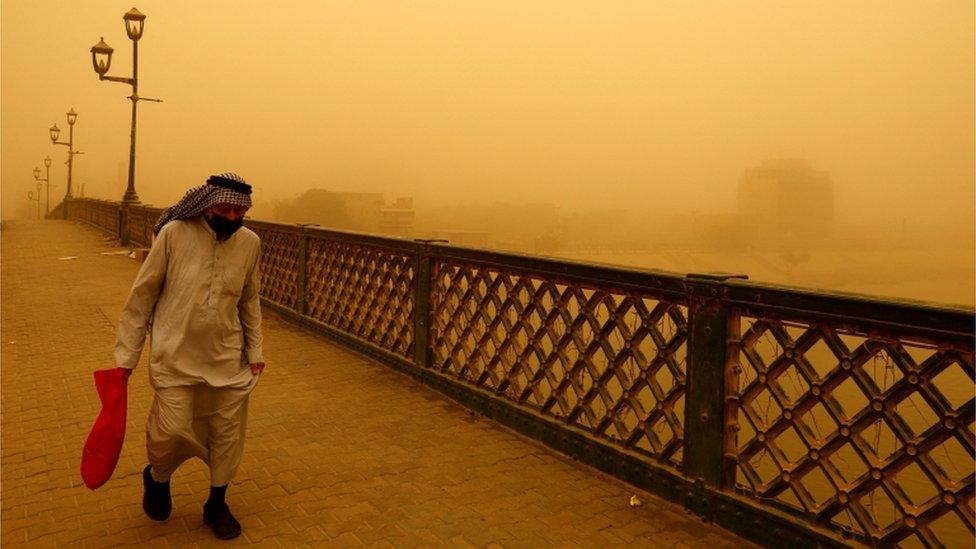 A man walks across a bridge in Iraq wearing a facemask.