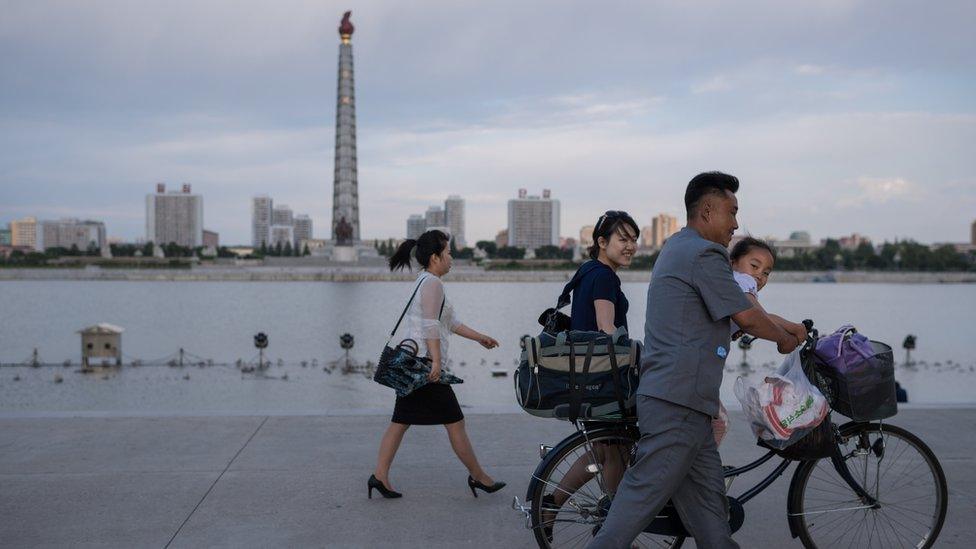 Pyongyangites go about their daily business with the Tower of Juche in the background