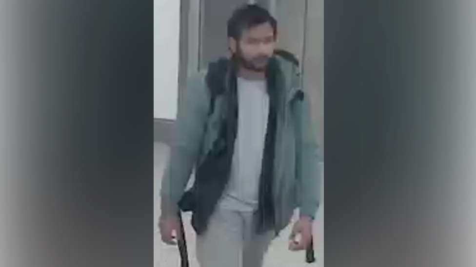 CCTV of Pankaj Lamba wearing a green coat, white top and grey pants. He looks to have a backpack and is walking. 