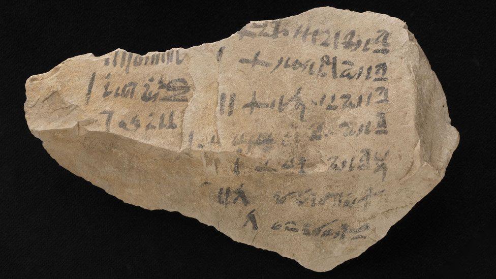 A receipt for making coffins 1530 to 1075BC made from limestone and with faded black ink writing. It is roughly diamond shaped and the writing is along its length. 
