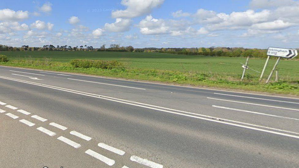 An empty road with a green field in the background and blurry sign. 