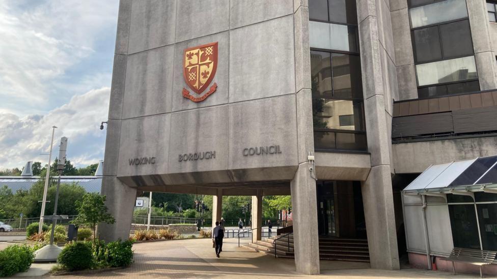 the outside of Woking council's headquarters, a tall grey concrete building with long columns of windows