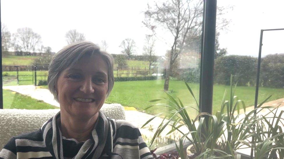 Sally Greenaway sitting in a lounge with a big window behind her and a pot plant to her left