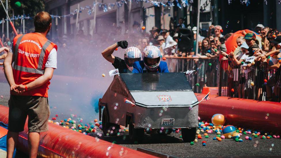 A silver Cybertruck running through colourful smoke