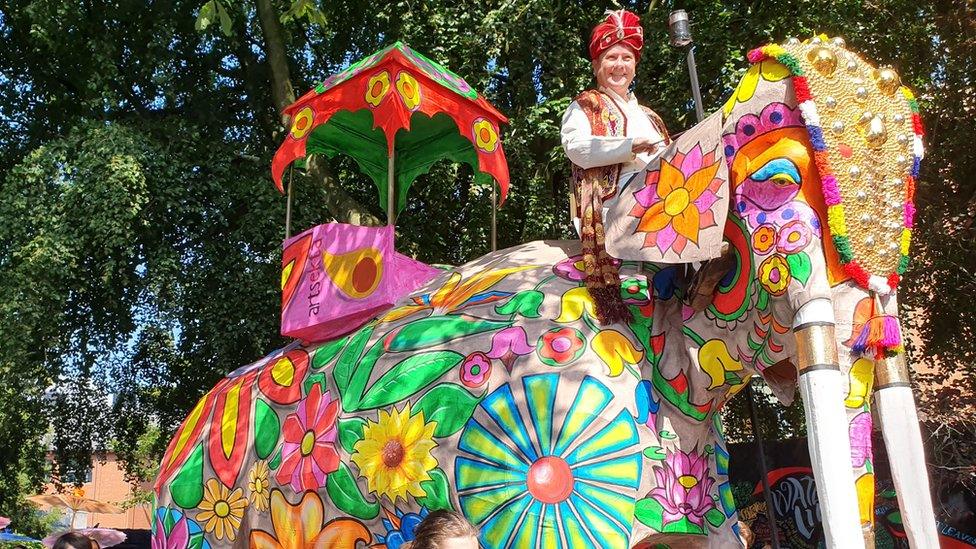 A man sits on an ornate papier-mâché elephant