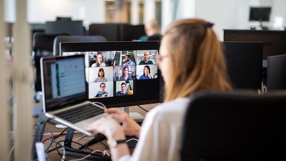 Rear view of a woman sitting in an office on a video call with team members