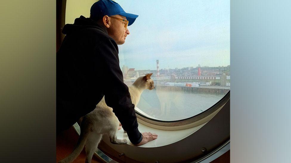 Adam Orpel and Felix the cat on a ferry looking out of the window