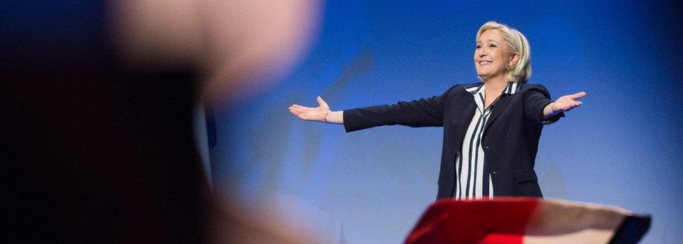 Marine Le Pen, beaming a smile with open arms, addresses an audience from a stage