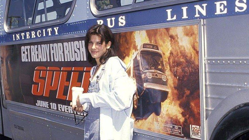 Sandra Bullock standing in front of a bus with a Speed movie advert