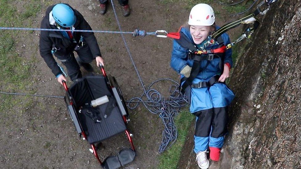 Inclusive climbing, Chloe is suspended by ropes and a harness as she is lowered into her wheelchair