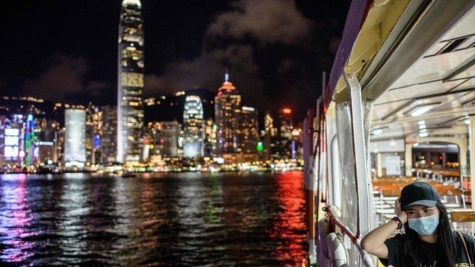 A woman wearing a face mask takes a Star Ferry in Victoria Harbour from Kowloon side to Hong Kong Island (back) on July 27, 2020